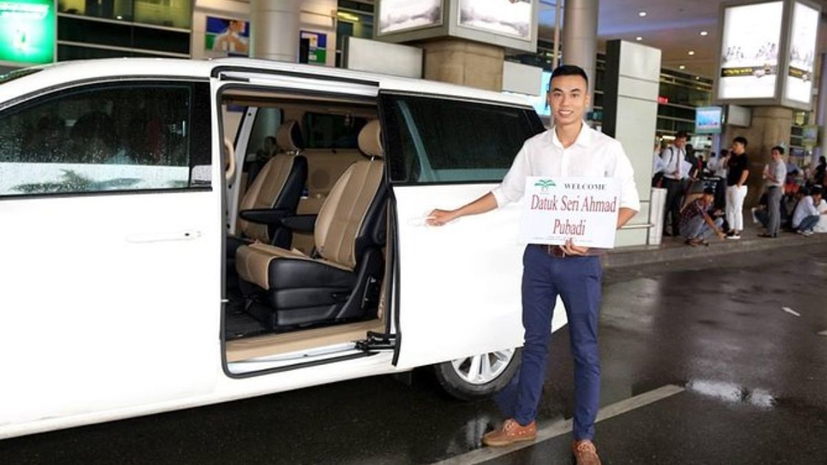 Private airport transfer service with a professional driver holding a welcome sign beside a white minivan outside the airport arrival terminal.