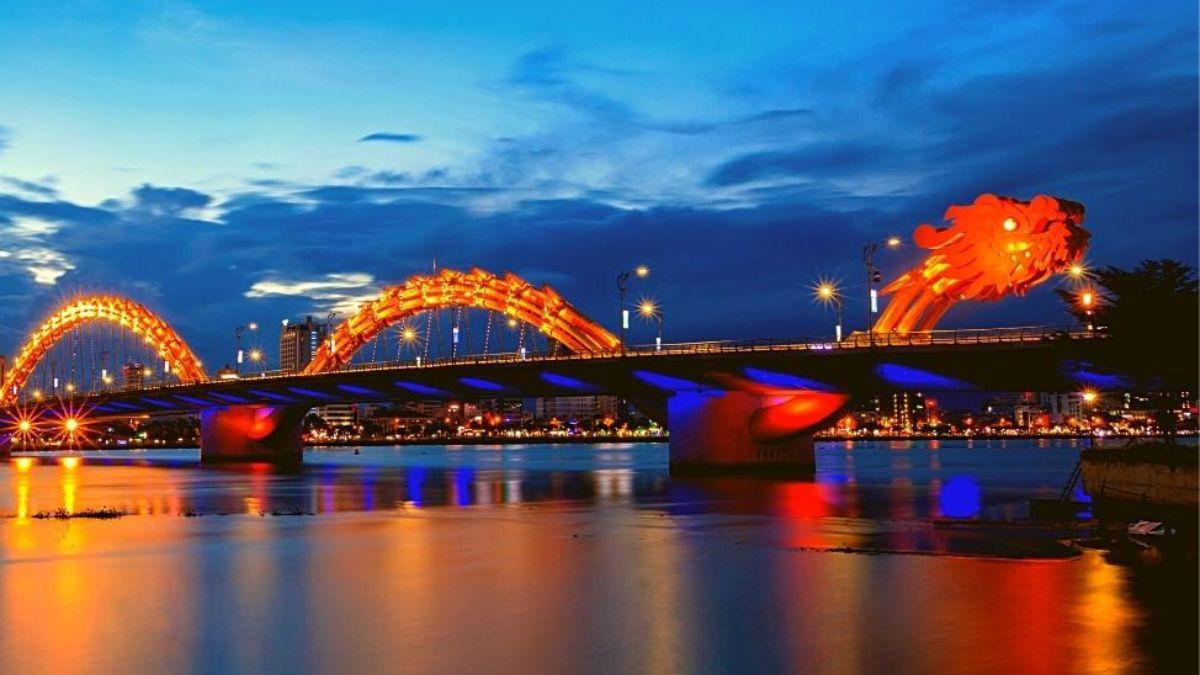 Dragon Bridge illuminated at night over the Han River in Da Nang, Vietnam, with colorful lights reflecting on the water.