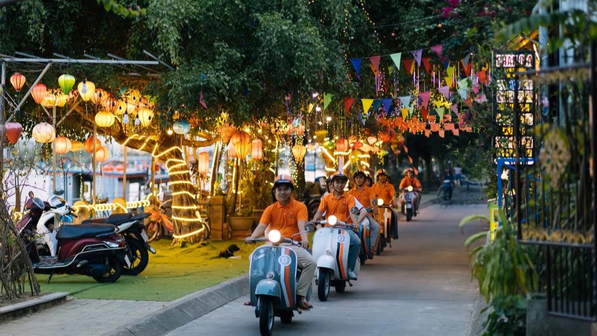 Travelers ride vintage scooters through the lantern-lit streets of Hoi An during an evening food tour by motorbike.