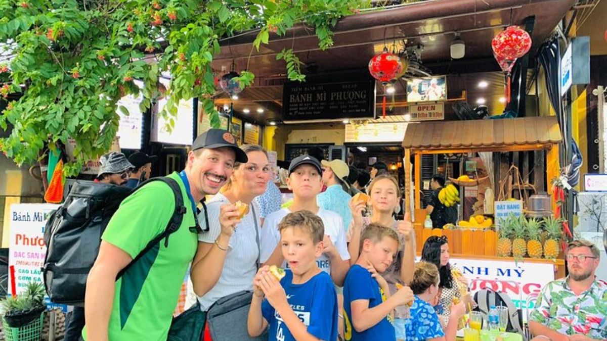 A family of tourists enjoys freshly made Vietnamese bánh mì in front of the famous Bánh Mì Phượng shop in Hoi An's Old Town.