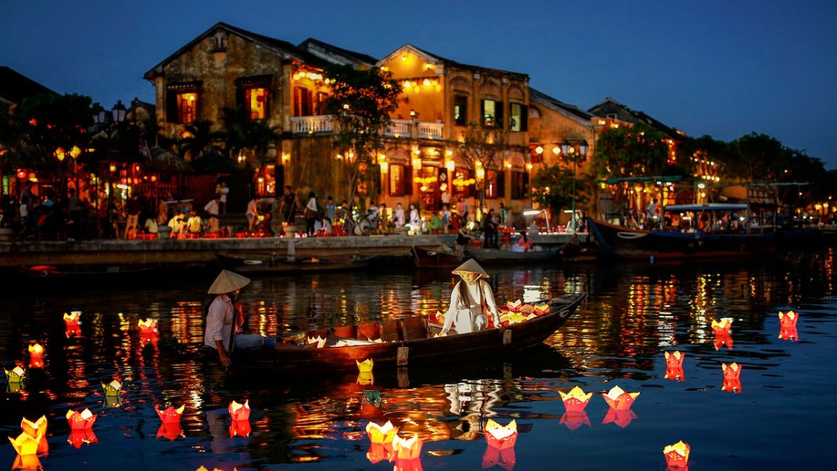 Traditional wooden boats carrying colorful floating lanterns on the Thu Bồn River in Hội An, Vietnam, at night.