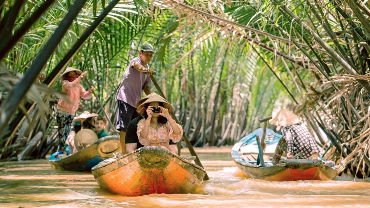 Tourists enjoy a traditional sampan boat ride through the narrow coconut-lined canals of the Mekong Delta, surrounded by lush nipa palm forests in southern Vietnam.