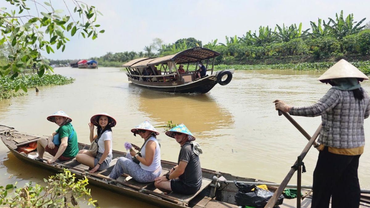 Foreign tourists enjoy a traditional sampan ride through fruit orchards on Tan Phong Island in Cai Be, Mekong Delta, Vietnam.