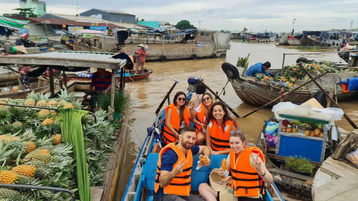Tourists wearing life jackets enjoy a boat tour through Cai Rang Floating Market, surrounded by boats loaded with fresh fruits and local produce in the Mekong Delta.