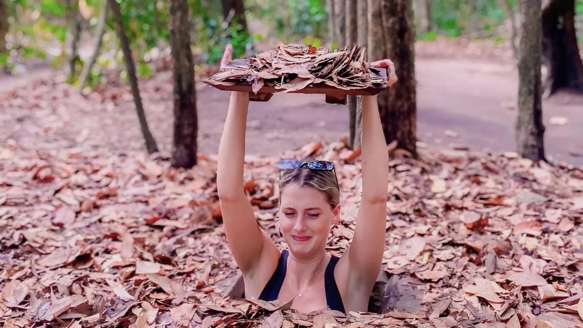 Tourist emerges from a hidden tunnel entrance while holding a camouflage cover at the Cu Chi Tunnels in Ho Chi Minh City, Vietnam.
