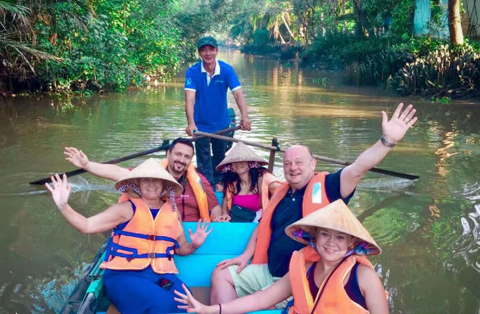 Tourists enjoy a traditional sampan boat ride through peaceful canals in the Mekong Delta, surrounded by lush coconut palms and tropical scenery.