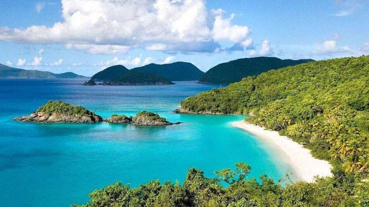 Crystal-clear turquoise water and white sandy beach at Quan Lan Island in Quang Ninh, surrounded by lush green hills.