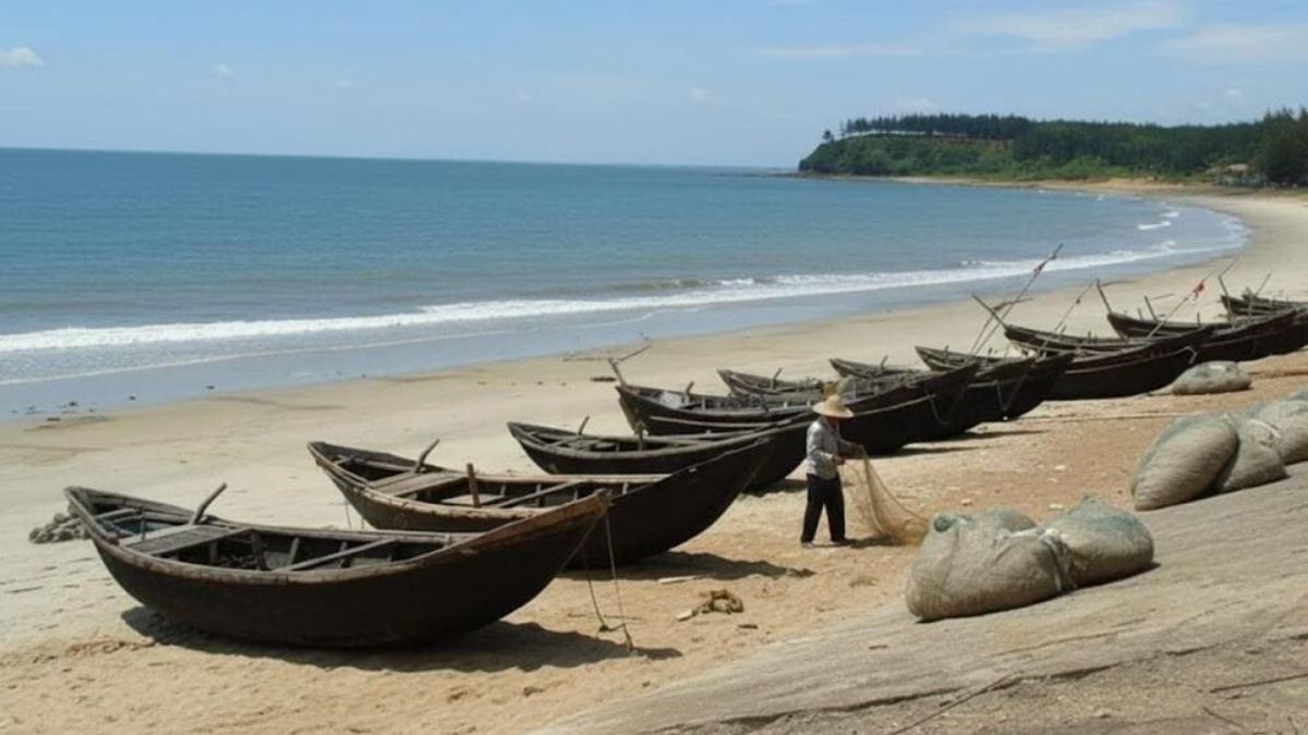 Visitors walking along the sandy shore of Quat Lam Beach in Nam Dinh during sunset with fishing boats in the distance