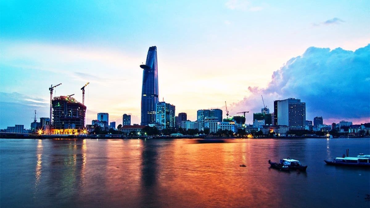 Panoramic view of the Saigon River at sunset, featuring the Ho Chi Minh City skyline with the iconic Bitexco Financial Tower reflected on the calm water.