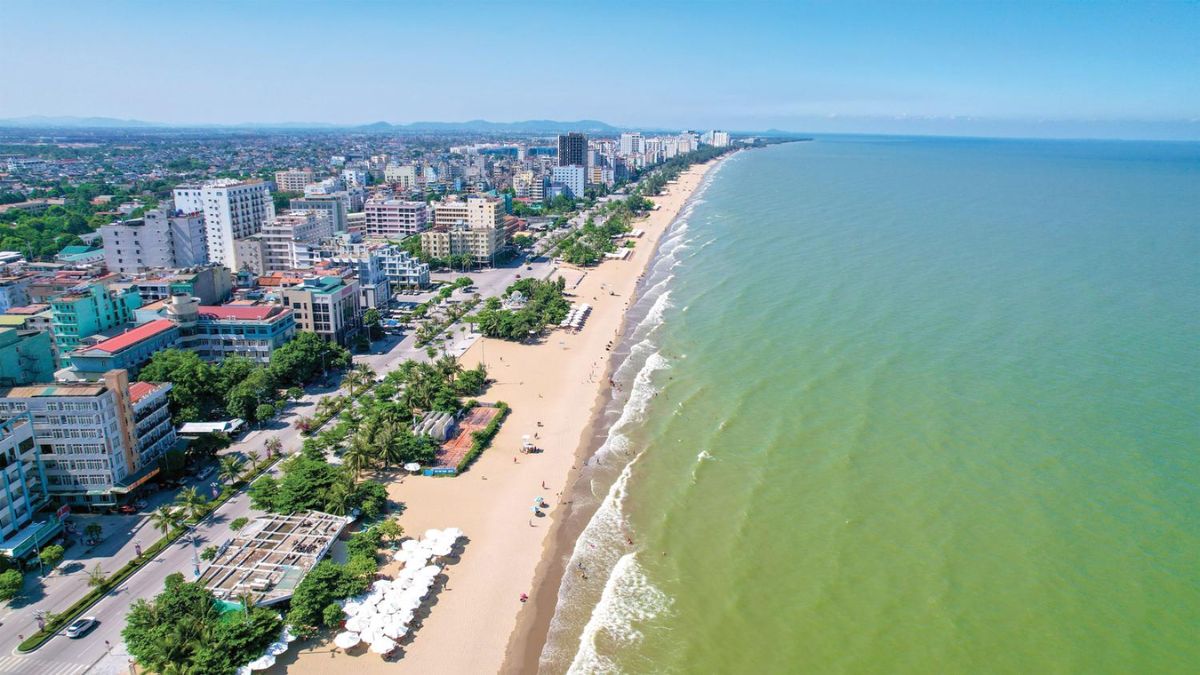 Wide sandy shoreline at Sam Son Beach, Thanh Hoa, with clear blue water, colorful umbrellas, and tourists enjoying the summer.
