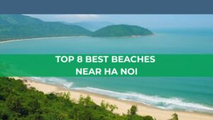 Top 8 Best Beaches Near Hanoi featured image showing a beautiful sandy beach with turquoise water, lush green mountains, and the title overlaid across the center.
