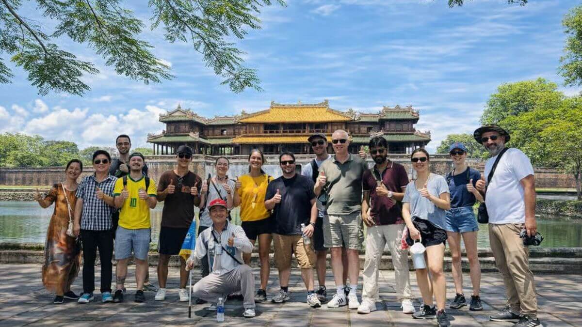 A group of tourists posing in front of a historic Vietnamese imperial palace on a sunny day.